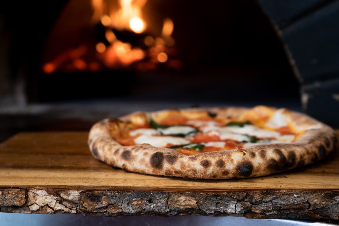 A pizza coming off the peel in front of the wood-fired oven